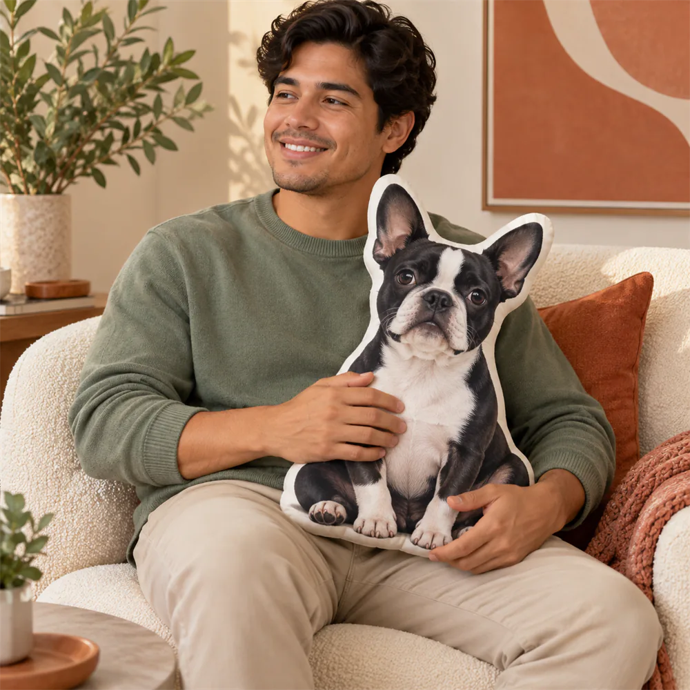 Man holds a medium Boston Terrier-shaped pillow on his lap.